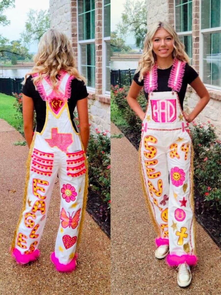 A young woman showcasing her brightly decorated senior overalls, front and back views, adorned with vibrant symbols, letters, and pink fringe.